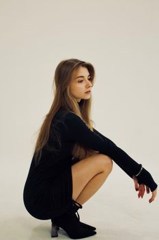 Crouching woman in black dress posing in a minimalist white studio.