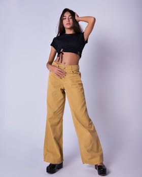 Young woman posing confidently in studio wearing black top and beige flared pants.