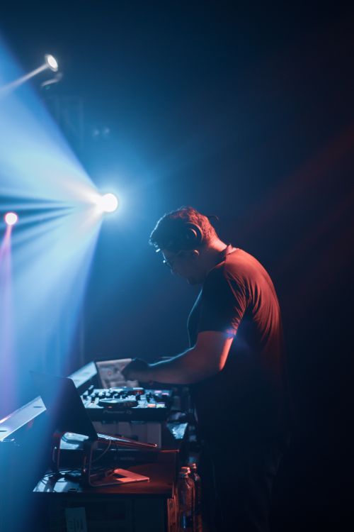 Free DJ immersed in mixing music with colorful stage lights creating an electric atmosphere. Stock Photo
