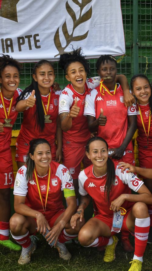 Free Smiling female football team in red uniforms celebrating victory with medals. Stock Photo