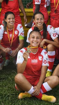 Women's football team posing with medals, celebrating victory outdoors.