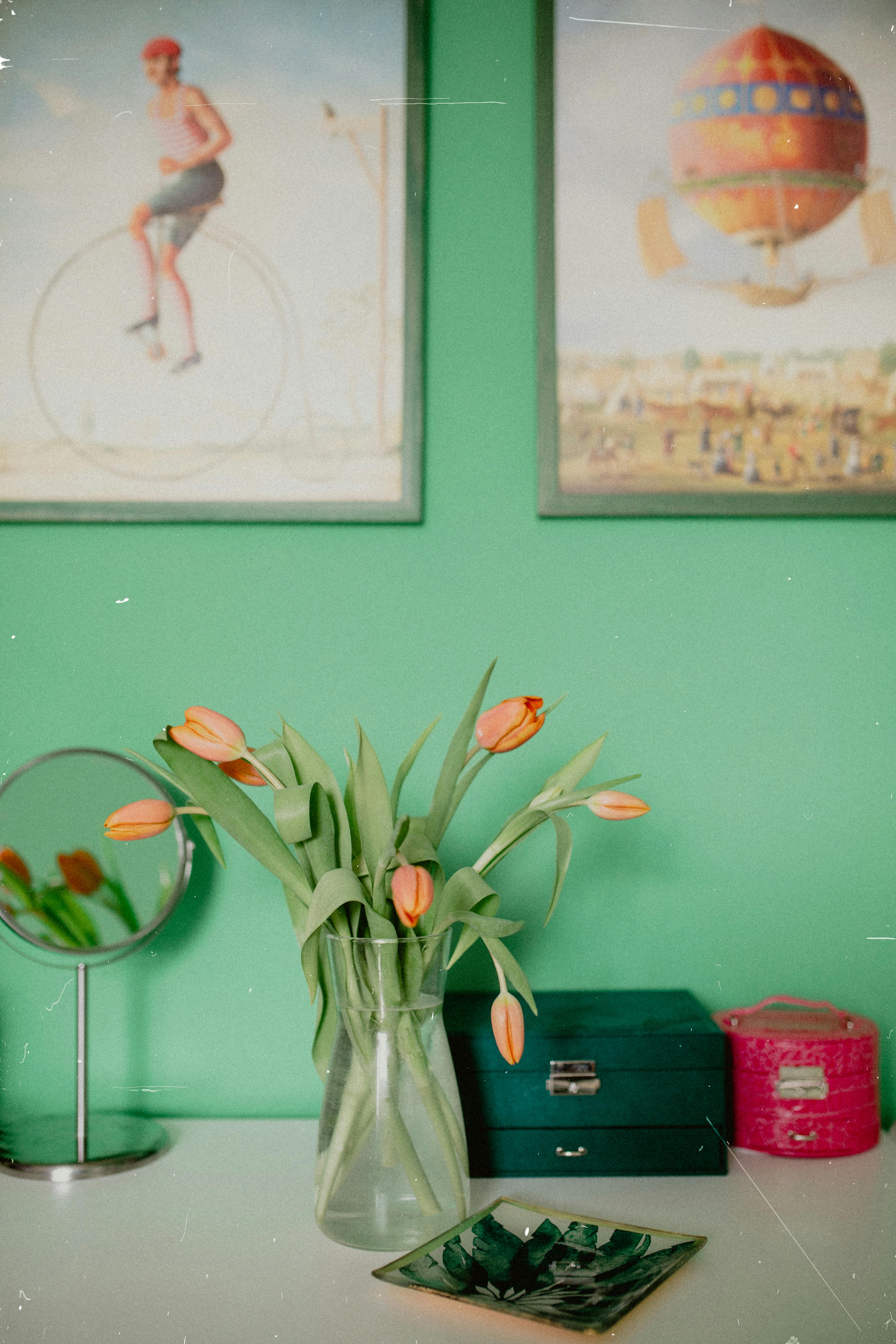 A stylish room featuring a bouquet of tulips in a vase, complemented by vintage art and vibrant decor on a dresser.