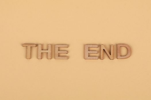 Wooden letters spelling 'The End' on a plain beige background, perfect for endings.