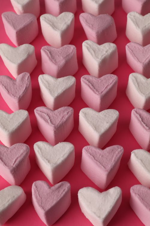 Free Heart-shaped marshmallows arranged on a vibrant pink background in a vertical pattern Stock Photo