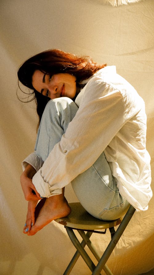 Young Brunette Sitting on a Chair with Her Legs Pulled Up to Her Chin 