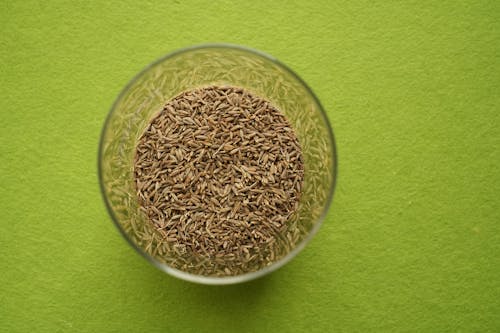 Free Cumin seeds in a jar with green background Stock Photo