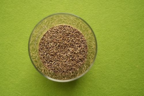 Free Cumin seeds in a clear glass bowl on a vibrant green background, viewed from above. Stock Photo