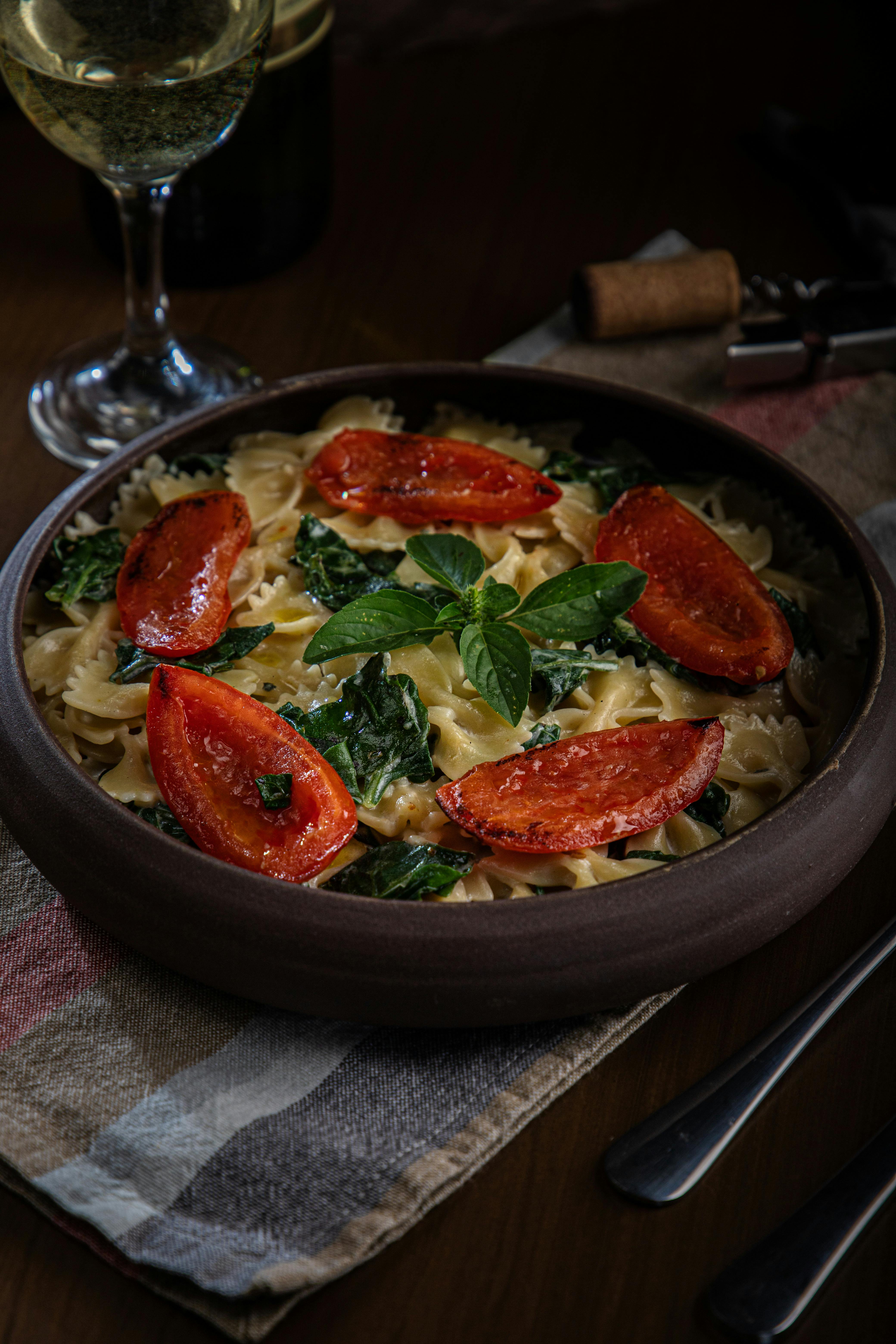 Delicious bowtie pasta with grilled tomatoes, basil, and spinach, served with white wine.