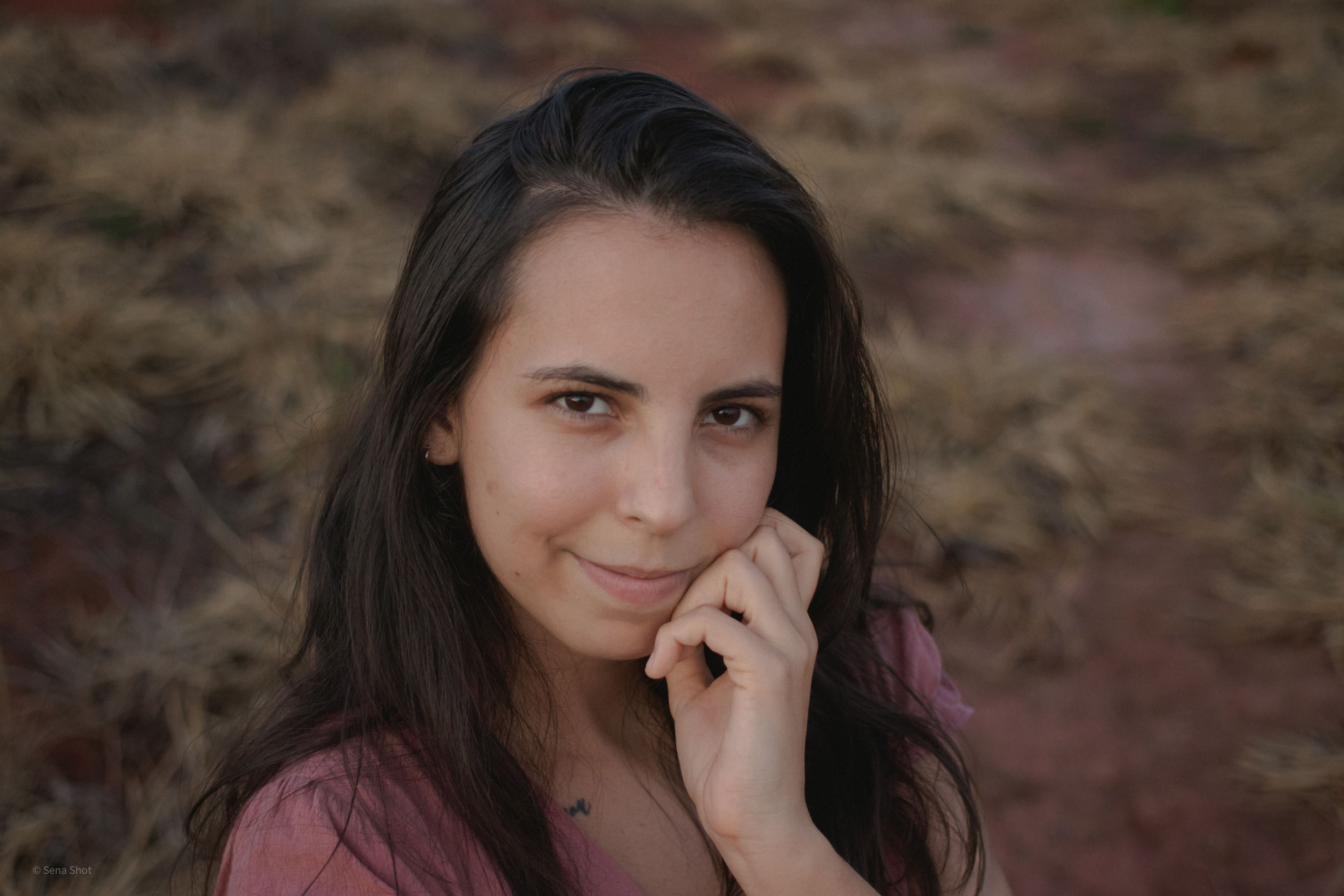 Portrait of a young brunette woman smiling in a grassy field during summer.