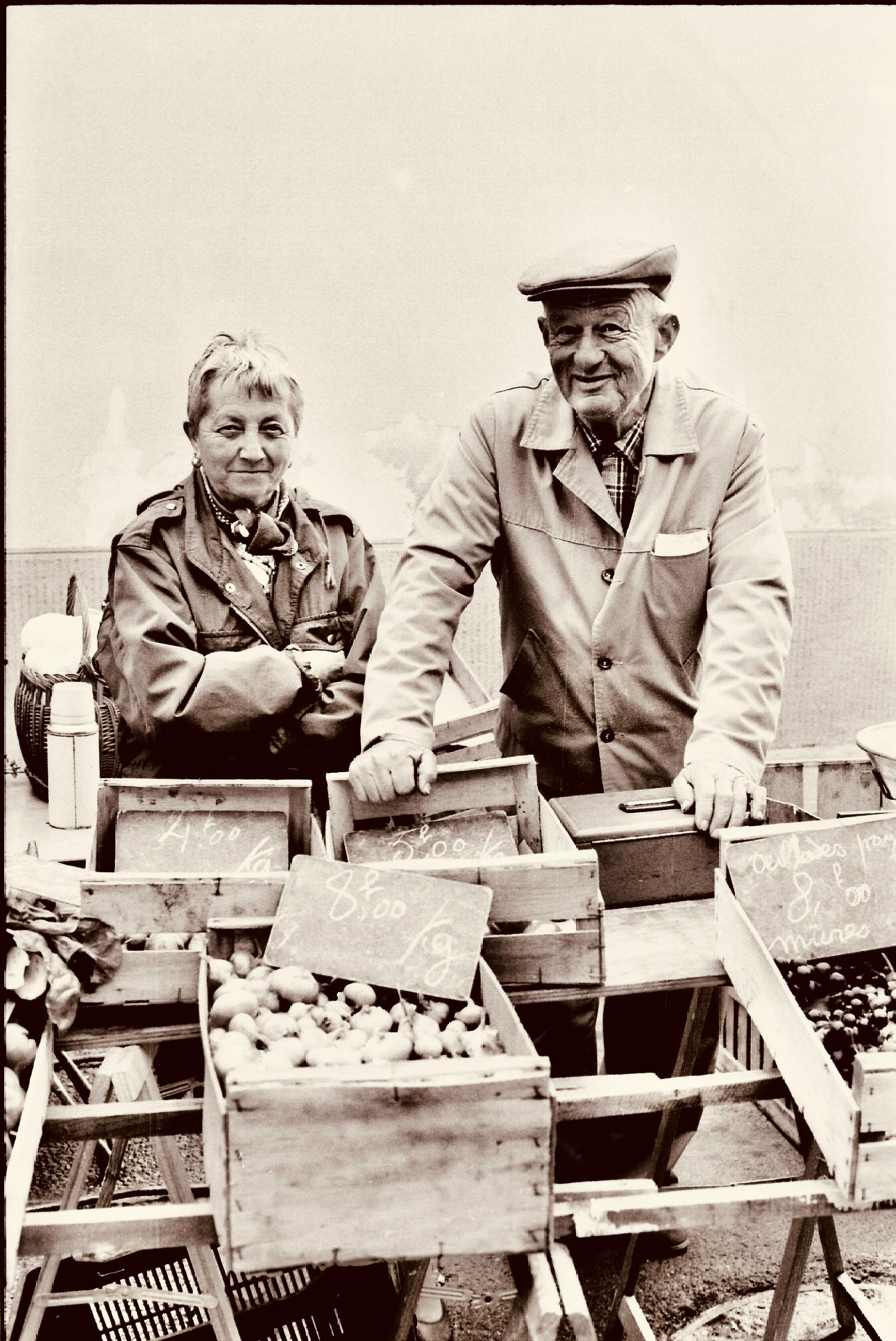 Charming elderly couple selling fresh produce at an outdoor market, captured in a vintage style.