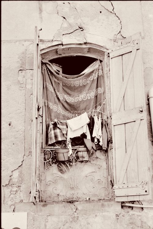 Free A rustic window with wooden shutters reveals hanging laundry and vintage charm. Stock Photo