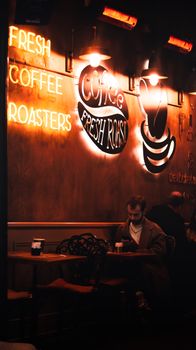 Warm café setting with neon lights, a man sitting and enjoying coffee.