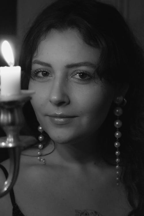 Black and White Photo of a Woman Wearing Pearl Earrings Standing next to a Candle 