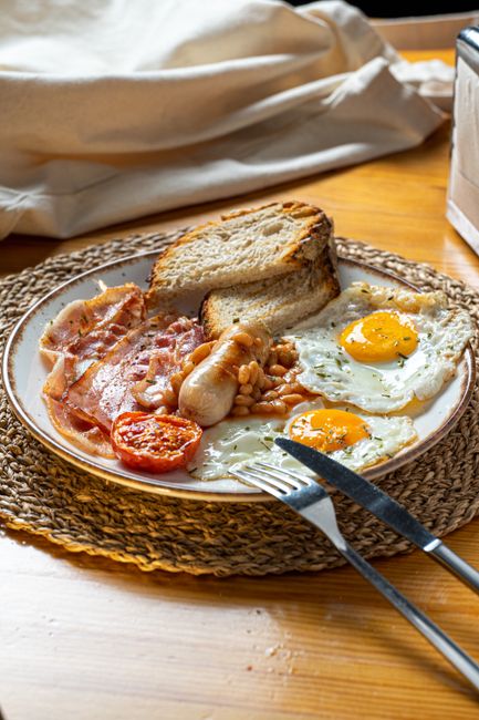 A tasty full English breakfast with eggs, sausage, bacon, beans, tomato, and toast.