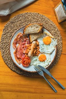 A traditional English breakfast featuring eggs, bacon, sausage, beans, and toast on a woven mat.