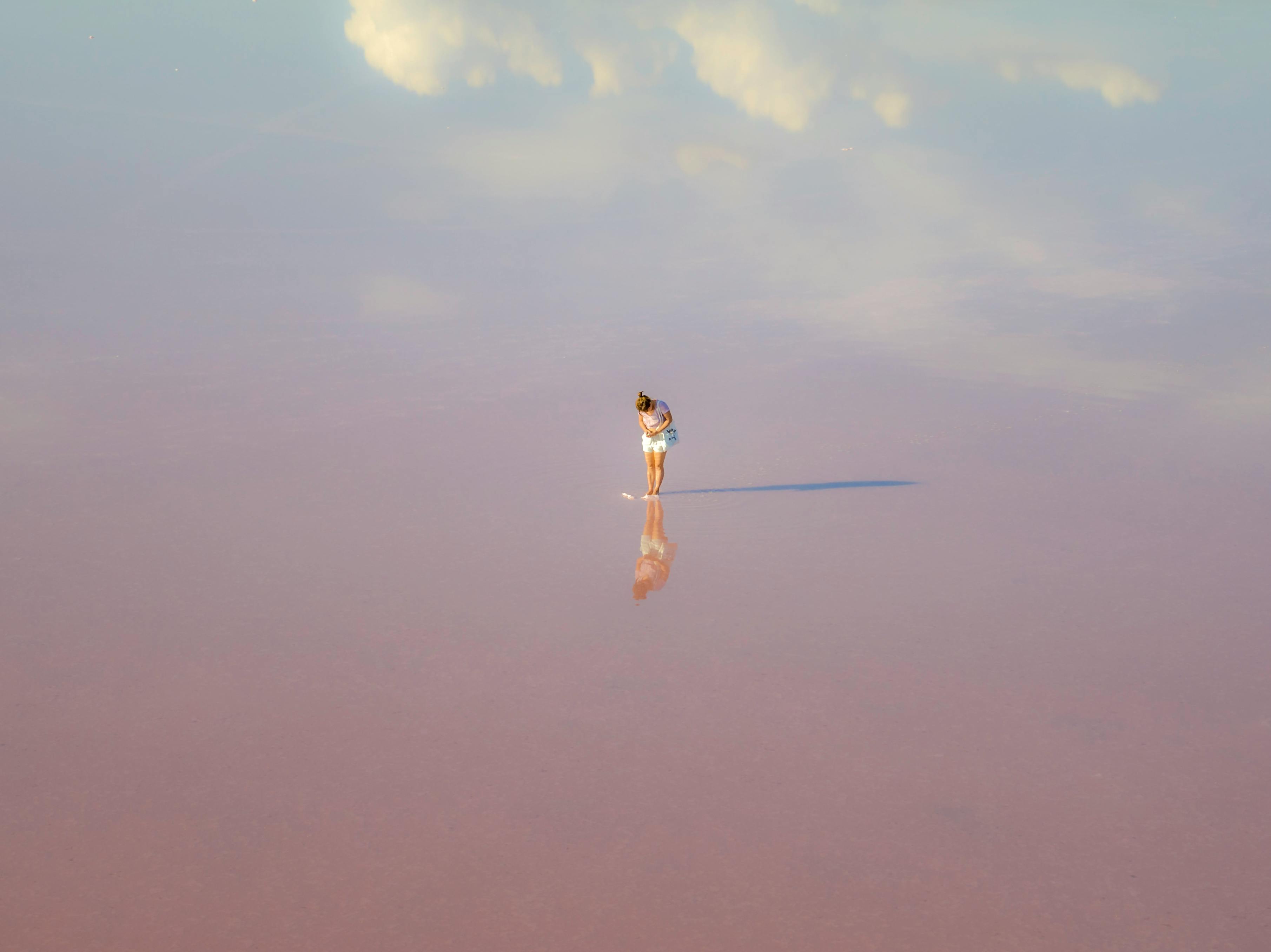 A woman stands reflected in the calm, pink waters of Dimboola's famous lake under a blue sky.