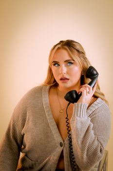Portrait of a stylish woman in a cozy sweater posing with a vintage telephone.