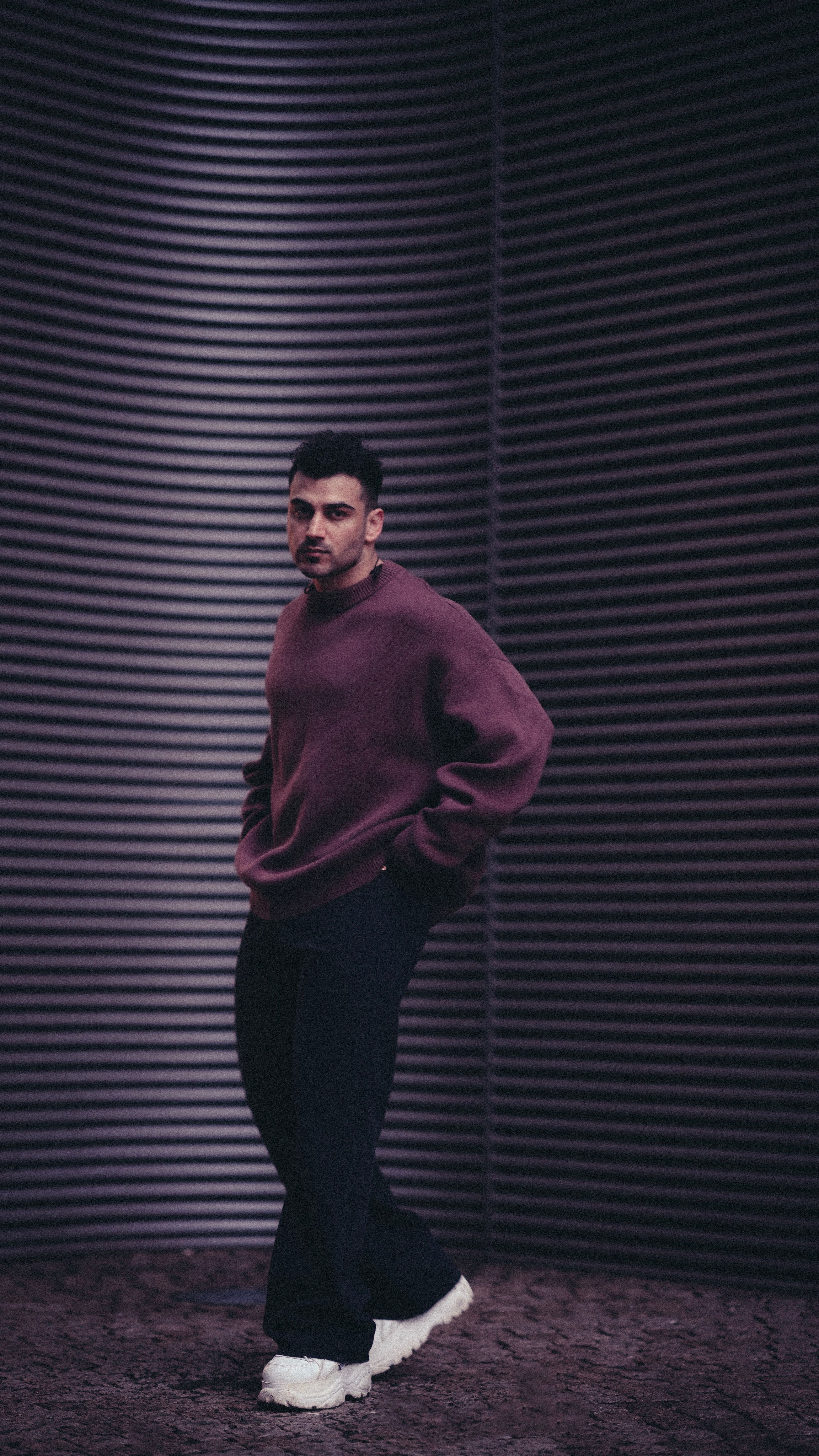Stylish man poses in trendy streetwear against corrugated metal backdrop in Berlin, Germany.