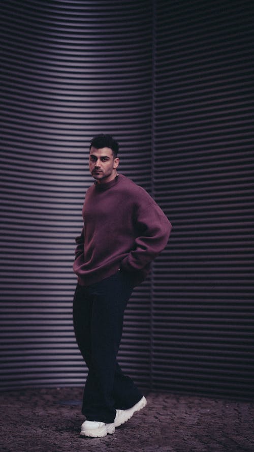 Young Man in a Streetwear Outfit Standing on the Background of a Modern Building Wall 