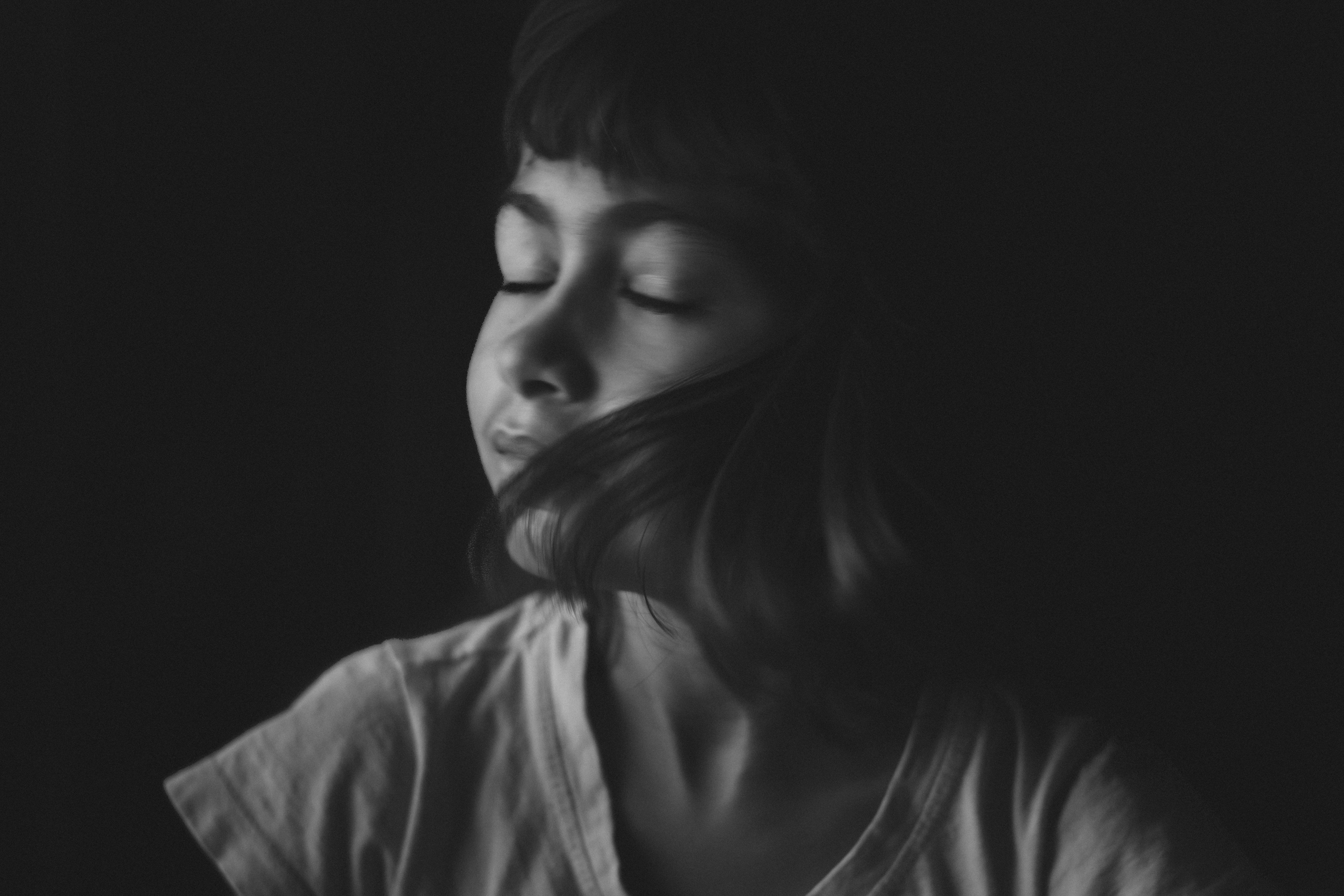 Artistic black and white portrait of a teenager with eyes closed and hair flipping.