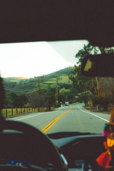 A picturesque road trip view from a car driving through lush green hills.