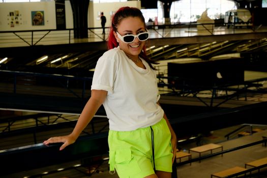 A stylish woman smiling in vibrant clothes, posing indoors in São Paulo.