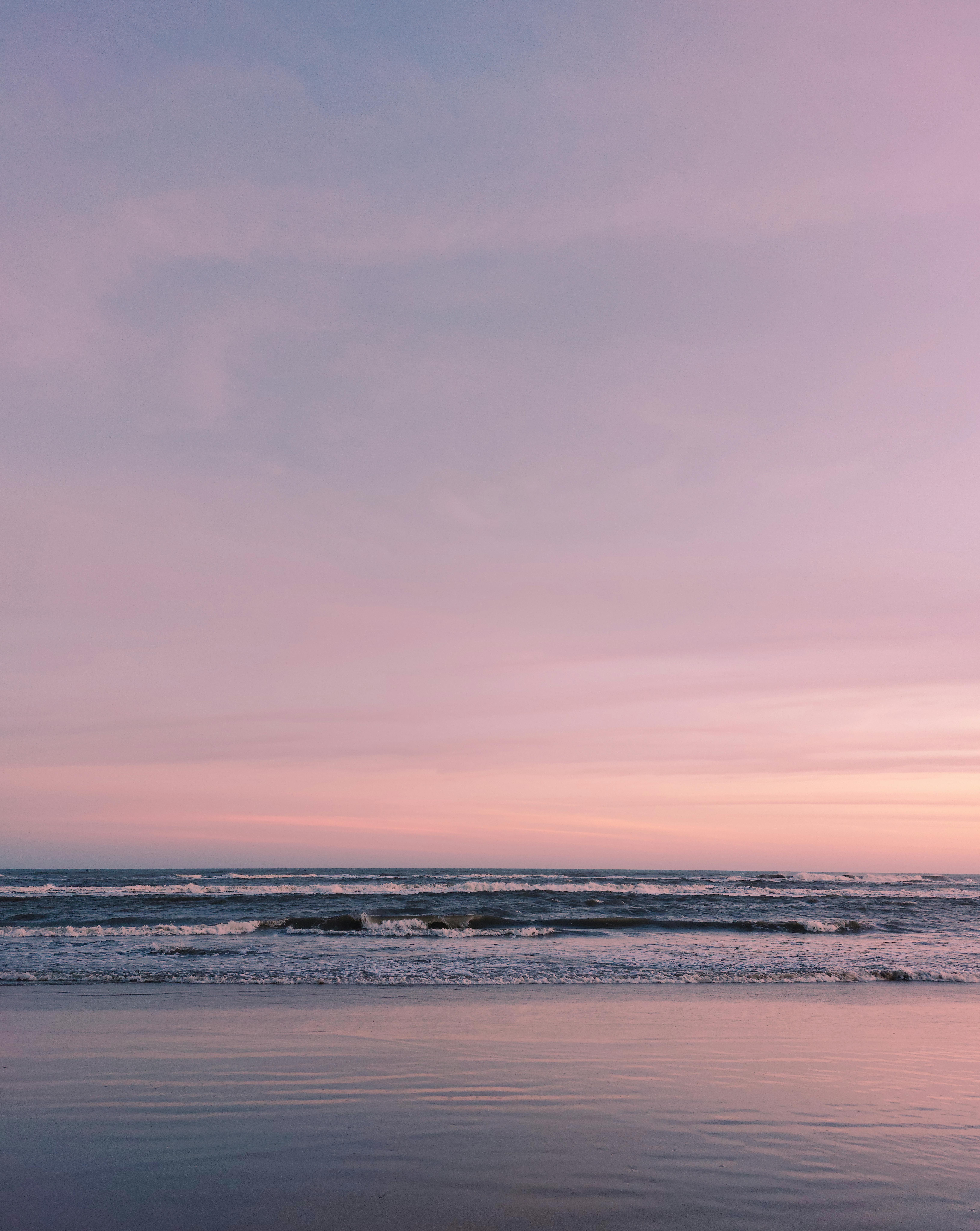 Peaceful ocean waves gently crash under a stunning pink sky at sunset, capturing a serene seaside moment.
