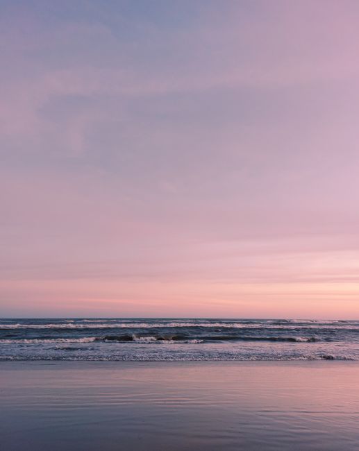 Peaceful ocean waves gently crash under a stunning pink sky at sunset, capturing a serene seaside moment.
