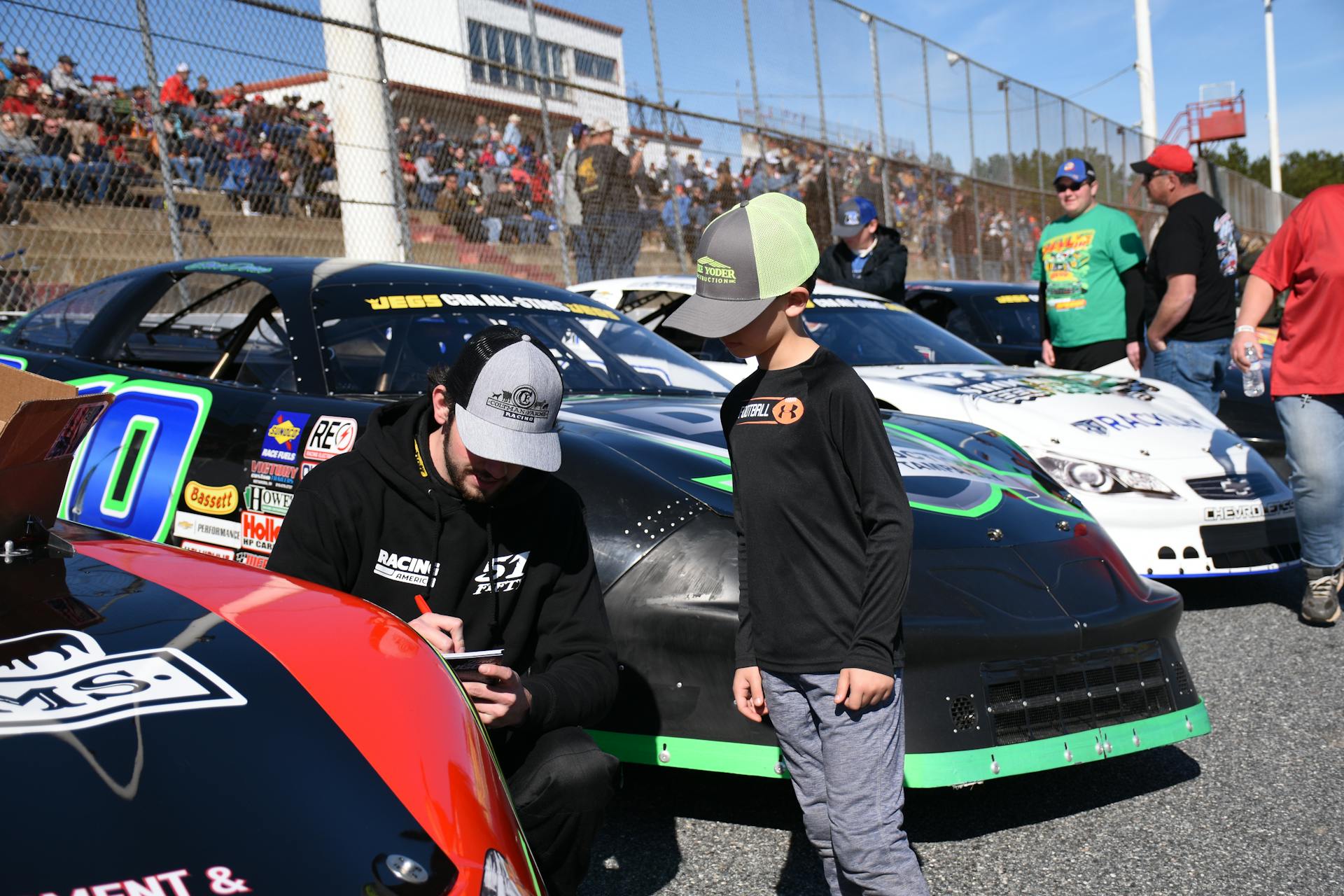 Racing Driver Signing Autograph to Boy near NASCAR Cars