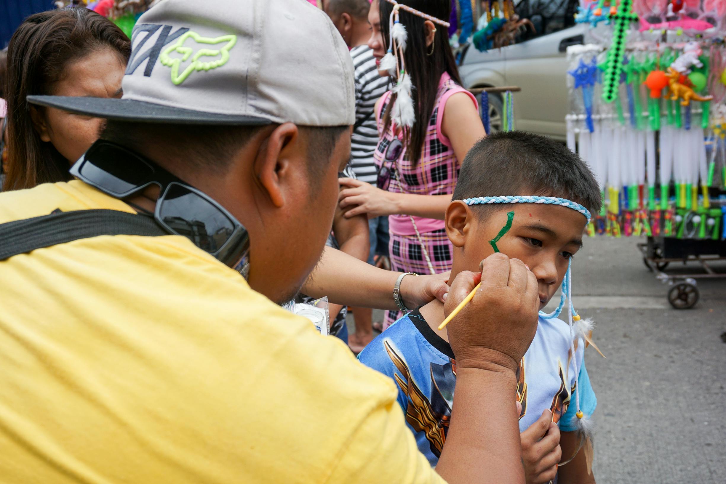 A child getting face painted at a vibrant street festival in Iloilo City, Philippines.