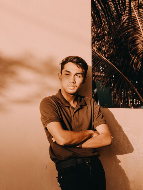 Free A young man with crossed arms leaning against a wall under warm sunlight, exuding a fashion-forward and relaxed vibe. Stock Photo