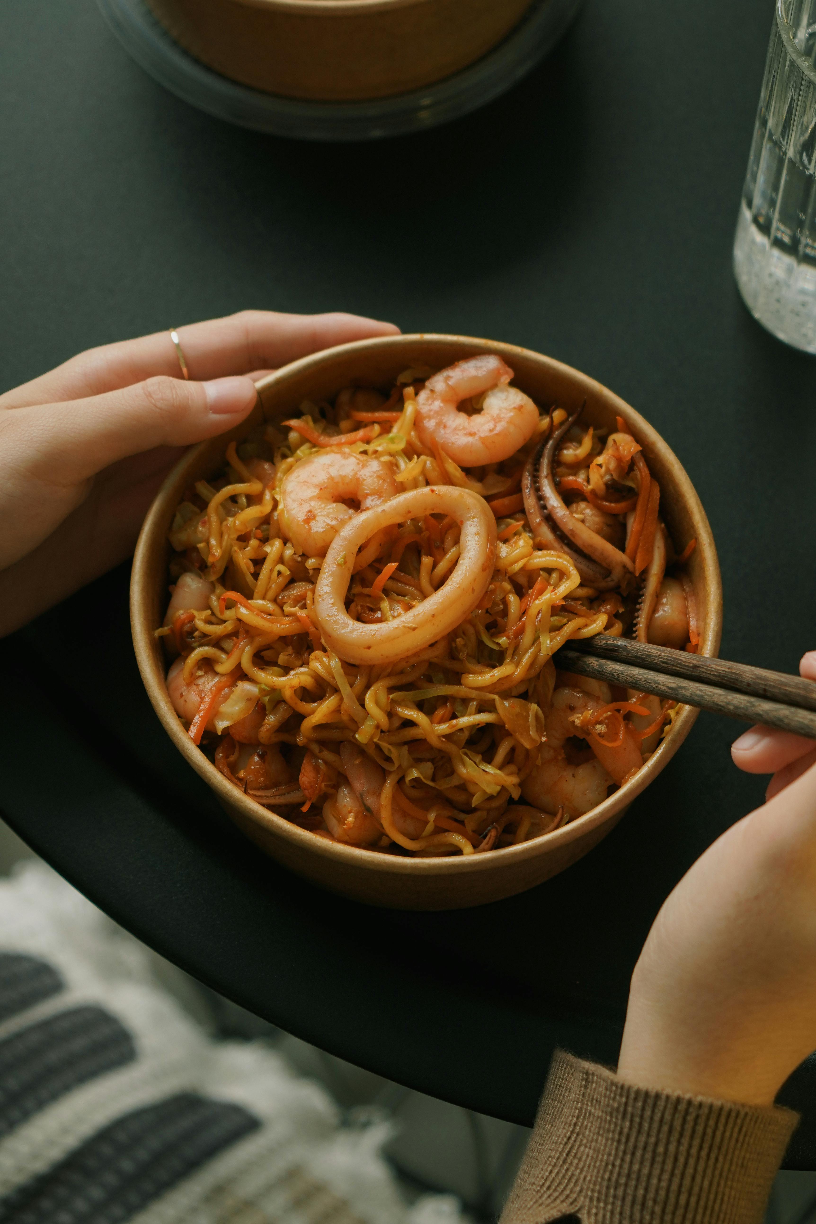 A warm and comforting bowl of seafood noodle soup featuring shrimp and squid, perfect for cozy indoor dining.
