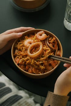A warm and comforting bowl of seafood noodle soup featuring shrimp and squid, perfect for cozy indoor dining.