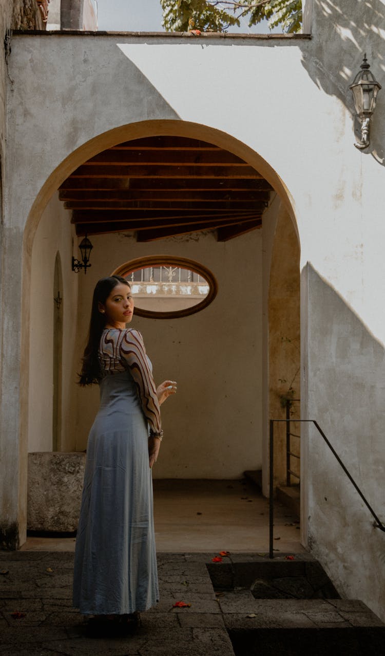 Young Beautiful Woman Standing In A Courtyard Wearing Blue Dress