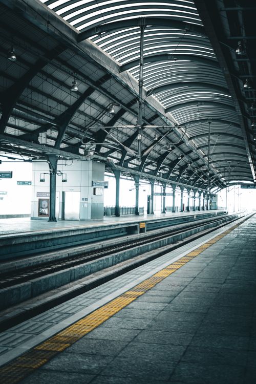 Free A spacious, empty train station platform with an arched roof and railway tracks. Stock Photo