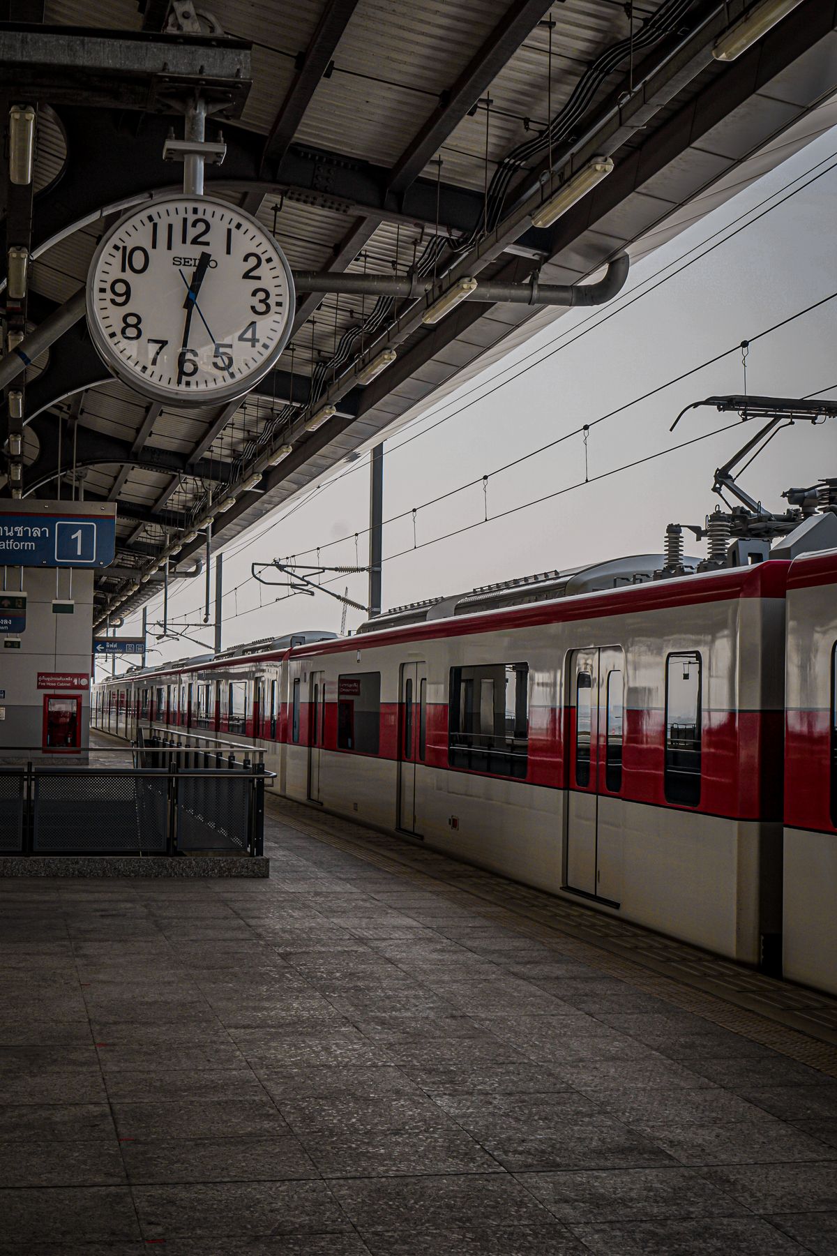 A train waits at a railway station platform with a large clock overhead. Illustrative editorial photograph.