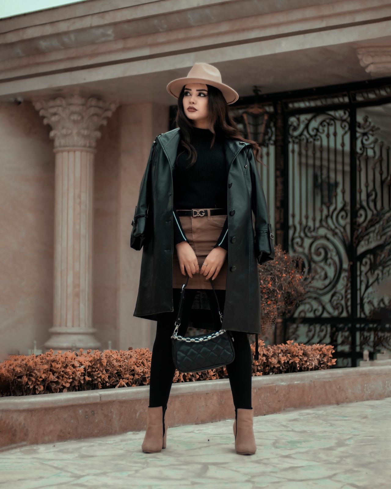 Woman in a black top, tan suede-look mini skirt, black trench coat and hat