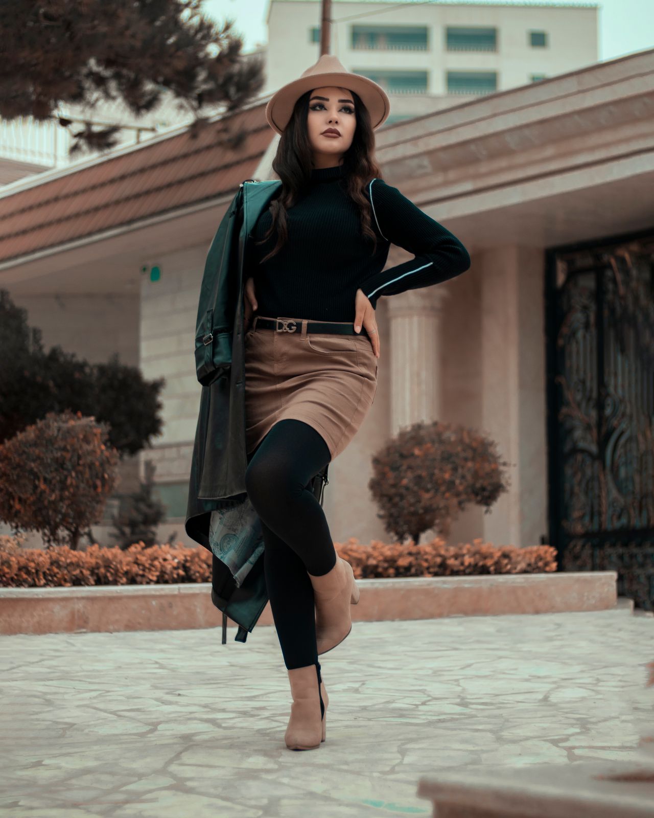 Woman in a black top and tan suede-look mini skirt with a hat outdoors