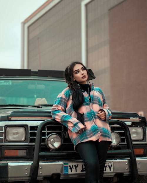 Female Model Wearing a Plaid Shirt Leaning on an Off-Road Car