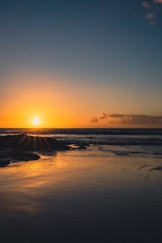 Tranquil beach sunset with golden sky and gentle waves, perfect for serene coastal scenes.