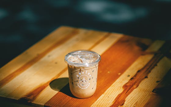 Refreshing iced coffee in a plastic cup on a wooden table with warm natural lighting.