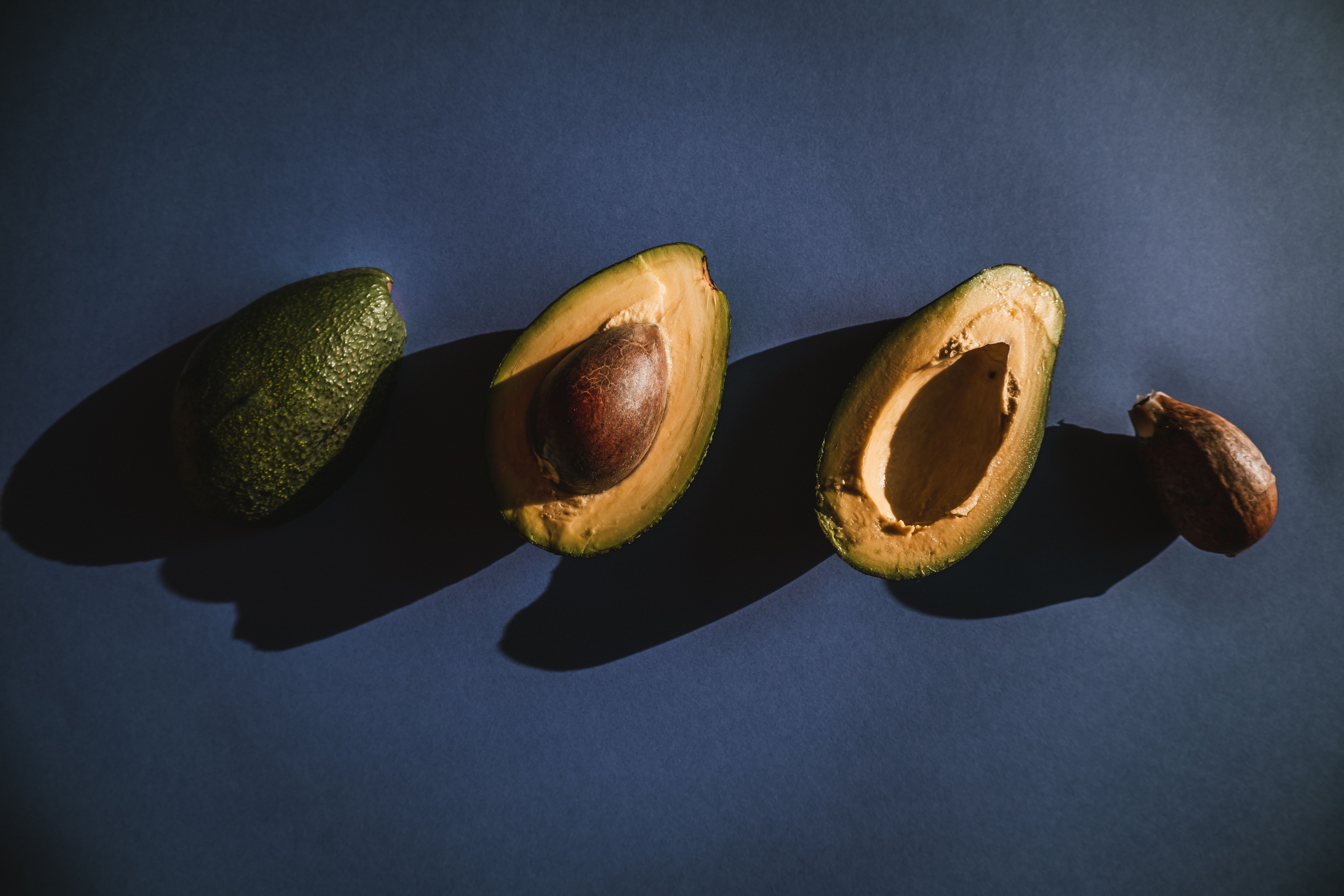 Overhead view of fresh avocados, halved and whole, with shadow play on a dark surface. - Evidence evidence guide for avocado cognition randomized trial