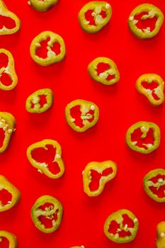 Top view of jalapeño slices on a bright red background, perfect for bold food concepts.