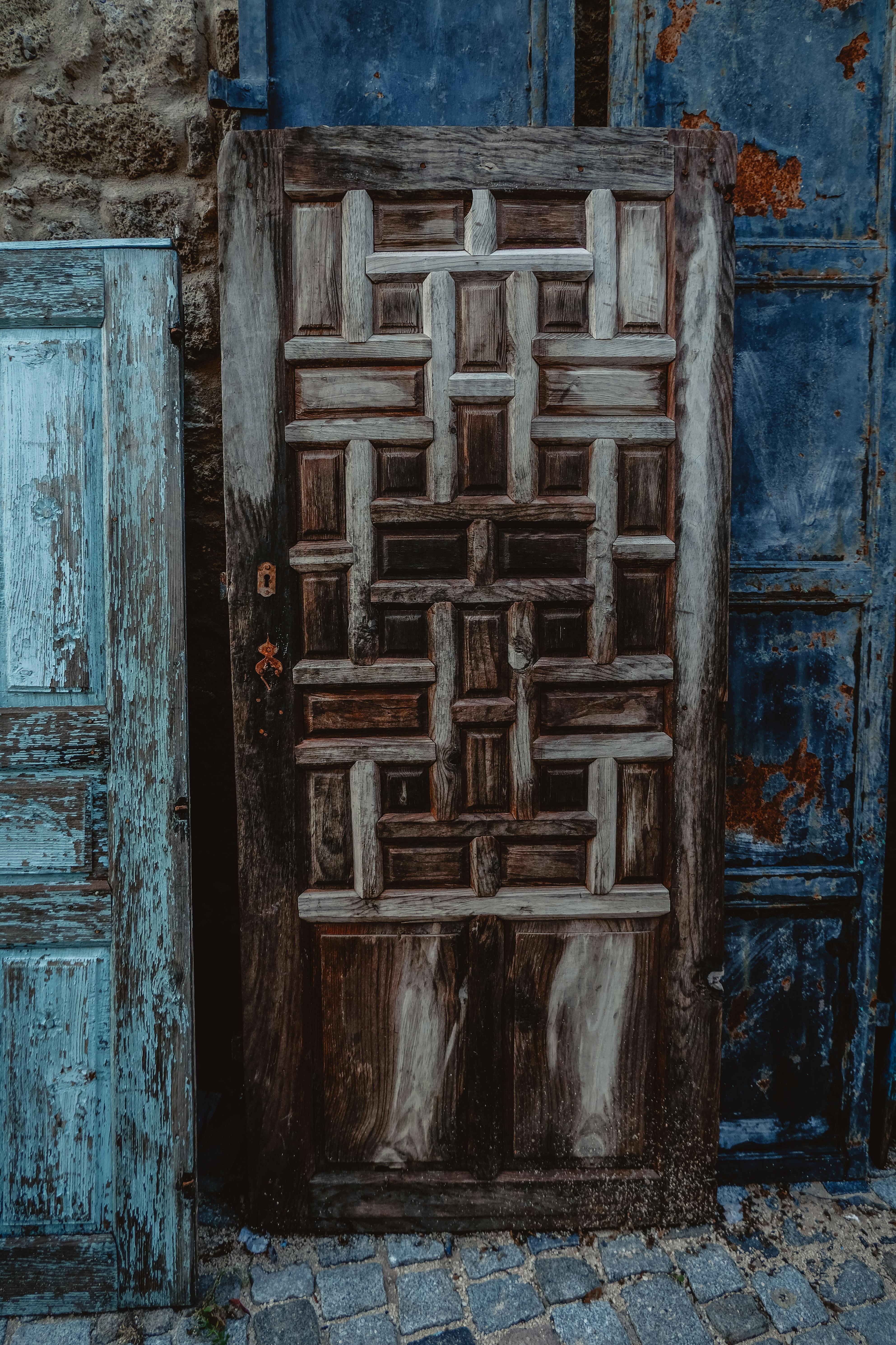 A rustic door with an elaborate geometric pattern, set against a weathered backdrop.