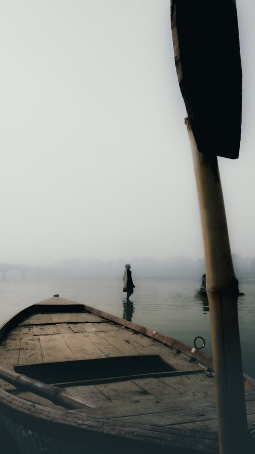 Free A serene foggy morning scene featuring a wooden boat and a figure on the Ganges River in Kanpur, India. Stock Photo