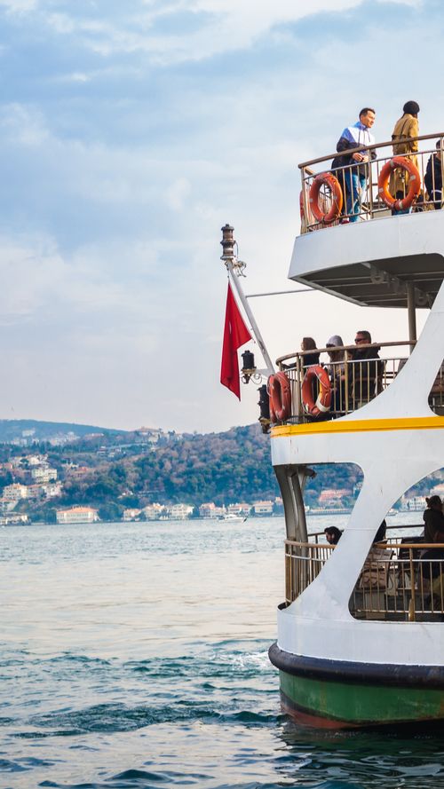 Free Scenic view of a ferry sailing along the Bosphorus with passengers onboard and distant urban landscape. Stock Photo