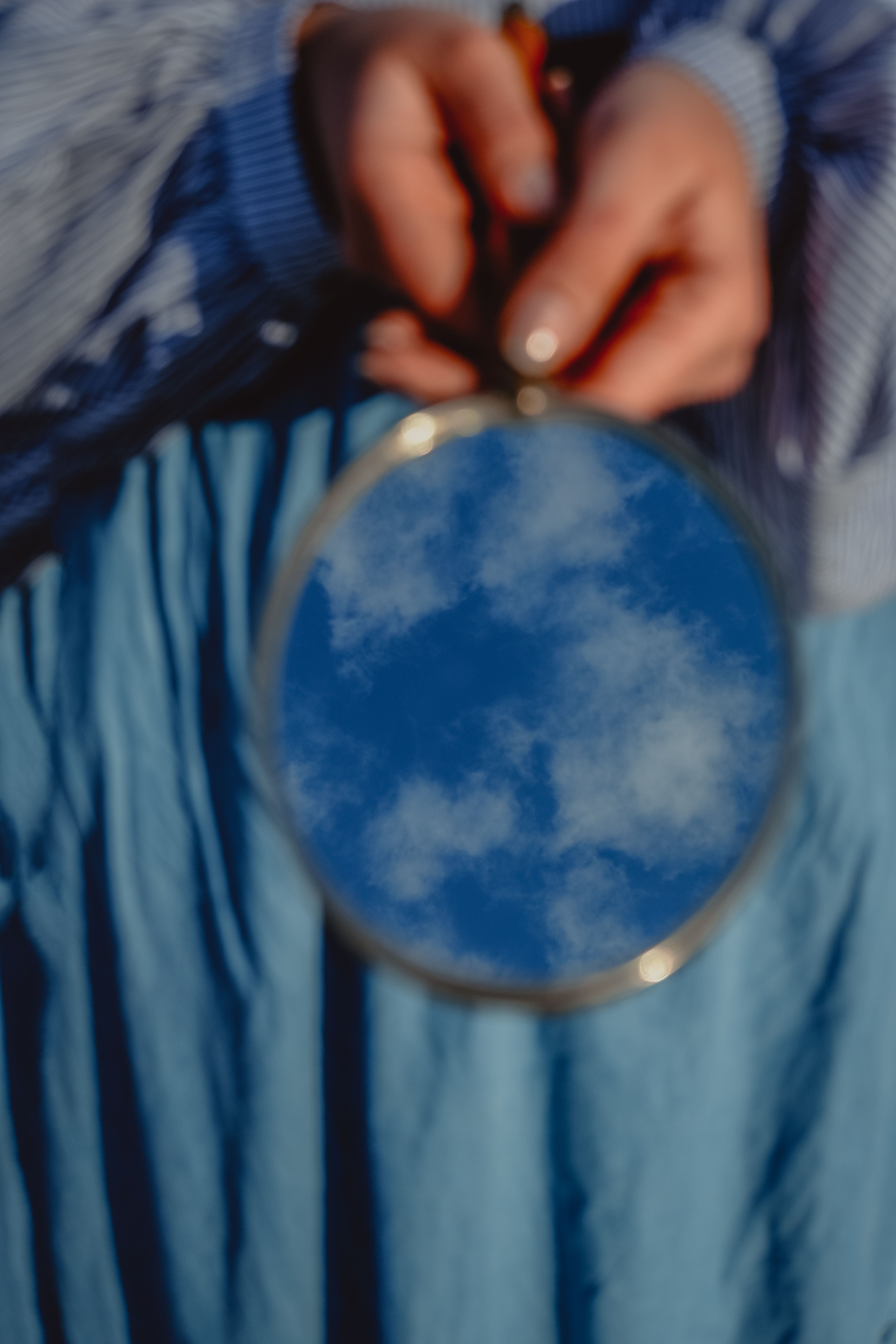 A person holds a mirror reflecting the sky and clouds, creating a dreamy illusion.
