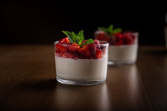 Short glasses of white panna cotta topped with chopped macerated strawberries and fresh mint