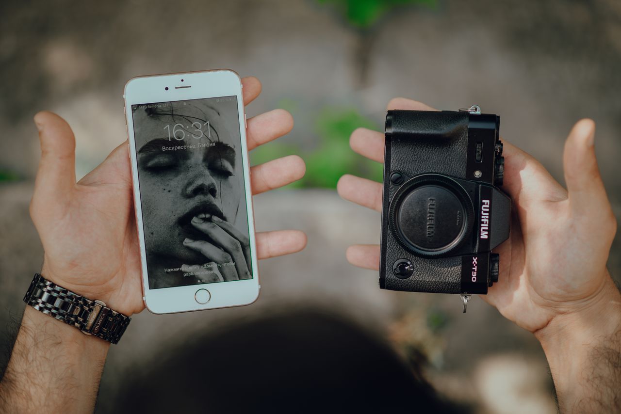 hands holding a smartphone with art wallpaper and a camera body outdoo