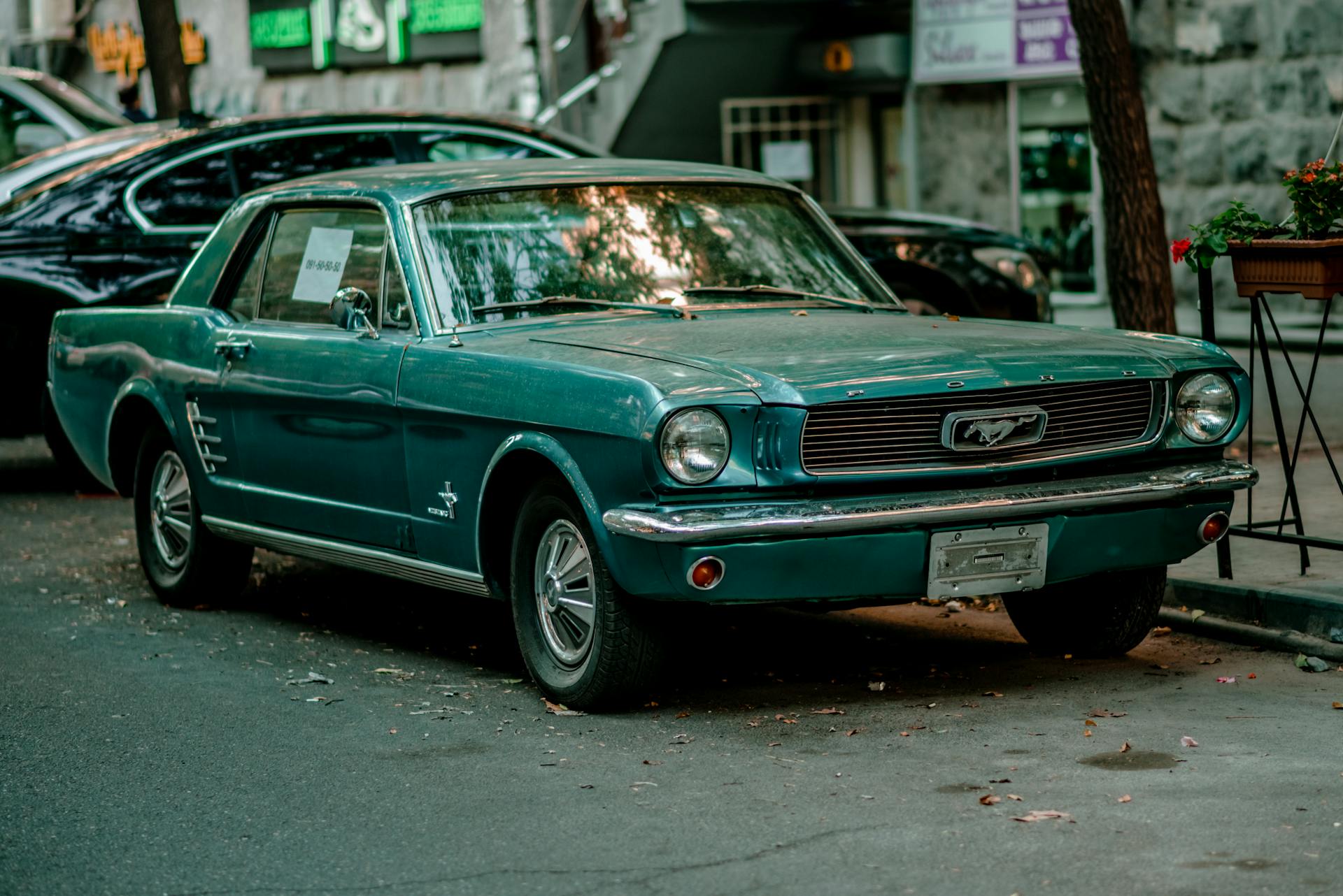 Classic teal Ford Mustang parked beside a sidewalk in a city setting, vintage appeal.